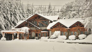 Una cabaña de madera con fachada de piedra, ventanas amplias y un tejado cubierto de nieve.