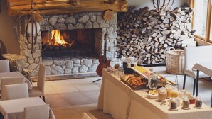 Un comedor con chimenea de piedra, mesas y un bufé con diversos alimentos.