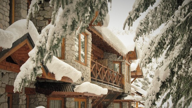 Un edificio de piedra con balcones de madera y árboles cubiertos de nieve.