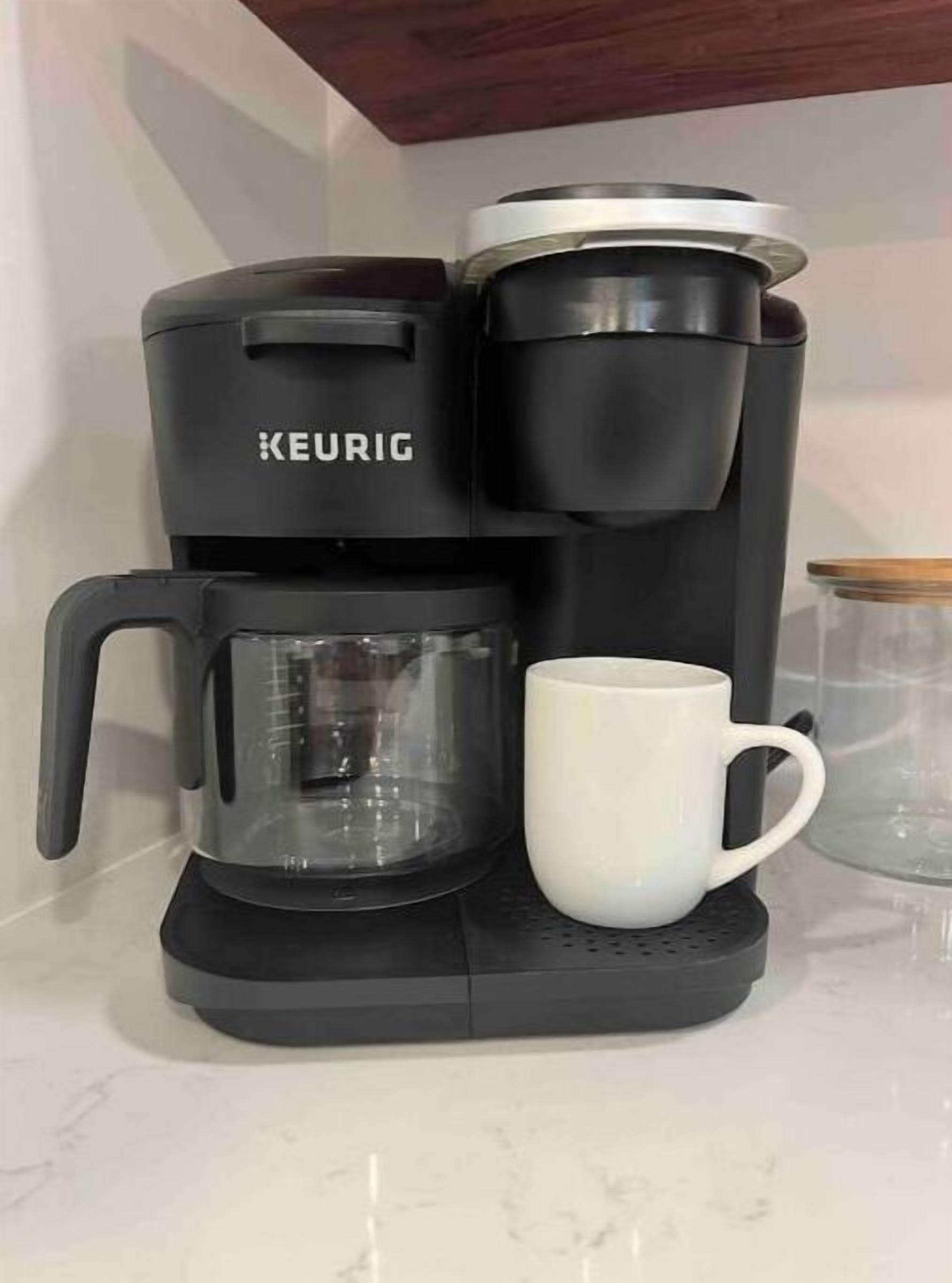 Una cafetera Keurig con jarra de vidrio y una taza blanca sobre una base negra.