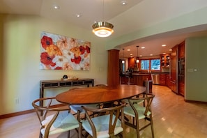 A spacious dining area with a wooden table and chairs, a large floral artwork on the wall, and a modern kitchen in the background.