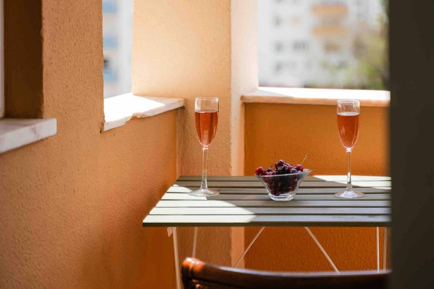Un balcón con dos vasos de una bebida rosada y un tazón de cerezas.