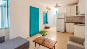 A modern apartment with a teal door, a kitchen with white cabinets, a dining area with a table and chairs, and a living room with a sofa. - Avlu Butik Otel Palamutbükü (Datça)