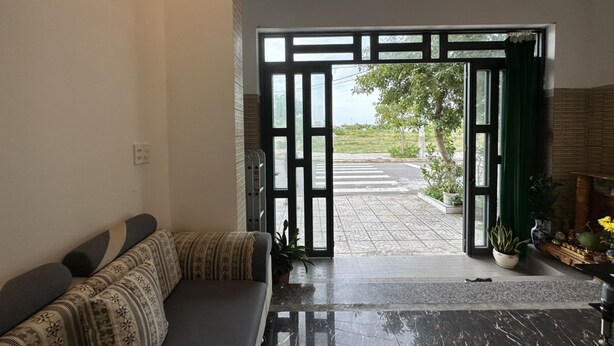 A room with a sofa, a potted plant, and a view of a street outside. - Ha Thu Motel (Da Nang)