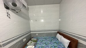 A small, neatly arranged room with a bed, a fan, and tiled walls. - Ha Thu Motel (Da Nang)