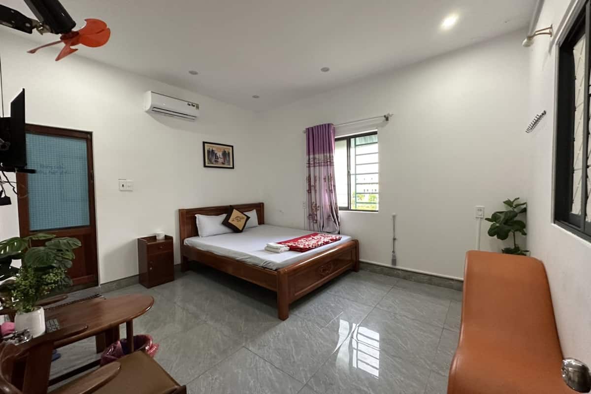 A bedroom with a bed, a desk, a chair, a window with curtains, a ceiling fan, and an air conditioning unit.
