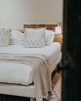 A neatly made bed with white bedding and two decorative pillows with zigzag patterns.