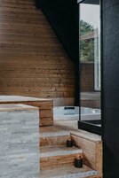 A modern bathroom with a wooden sloped ceiling, a stone countertop, and a glass shower enclosure.