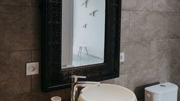 Un baño con un espejo grande, un lavabo redondo, una toalla y un inodoro.