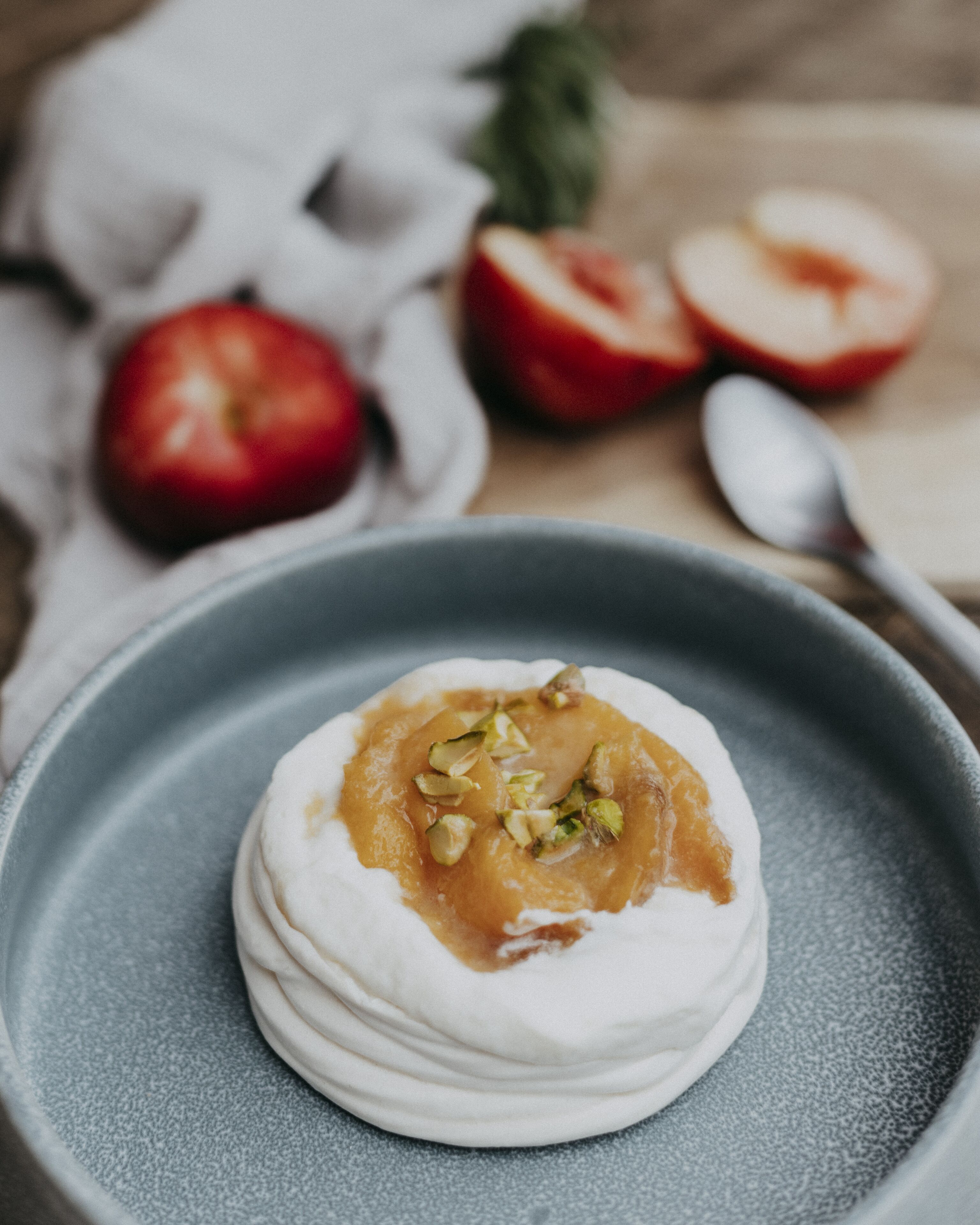 Un dessert présenté dans une assiette, avec une cuillère et des tranches de pomme en arrière-plan.