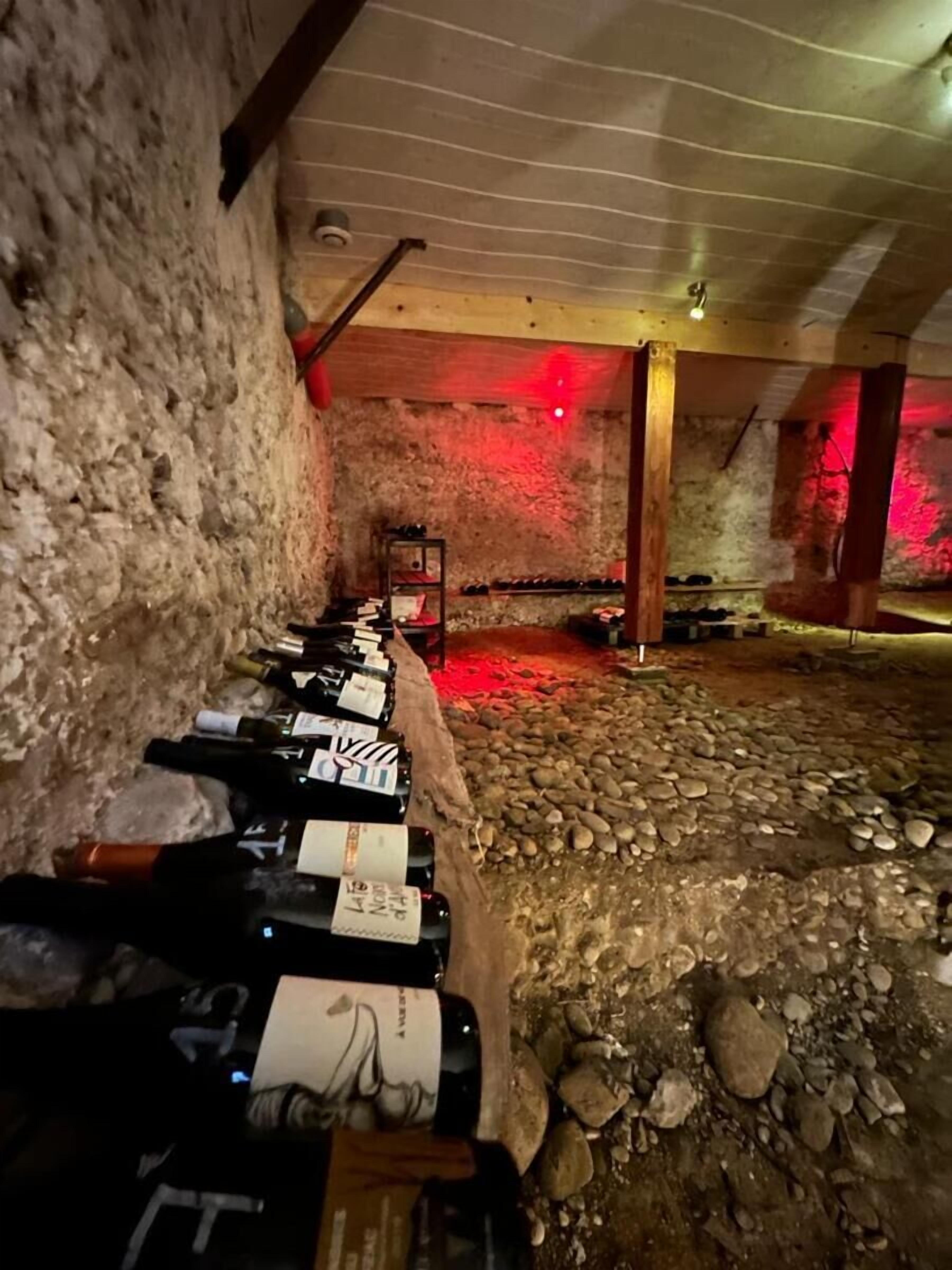 Une cave où les bouteilles de vin sont alignées contre le mur, un banc en bois et un sol en pierre.