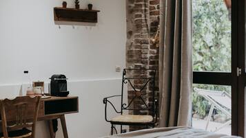 A room with a wooden desk, a chair, a bed, a window with curtains, and a brick wall.