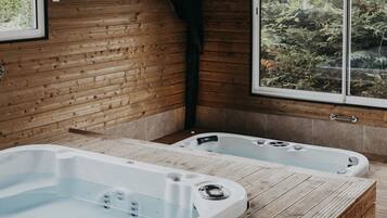 Una cabaña de madera con dos jacuzzis y un ventanal grande con vistas a un bosque.