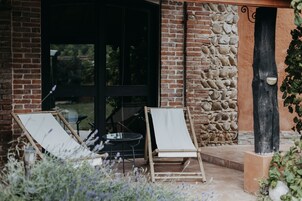 A patio with two wooden chairs and a small round table, a stone wall, and a glass door leading to the interior.