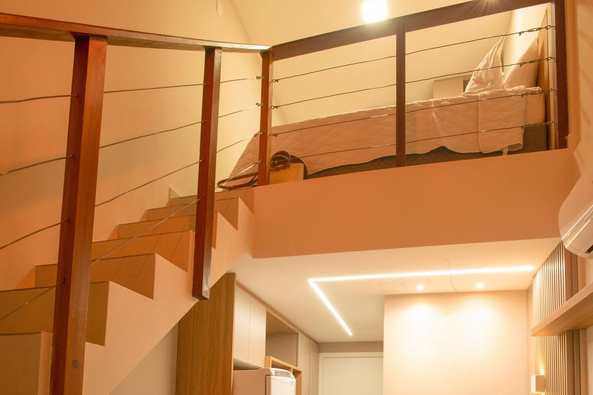 A modern apartment with a wooden staircase, a flat-screen TV, a dining area, and a sofa.