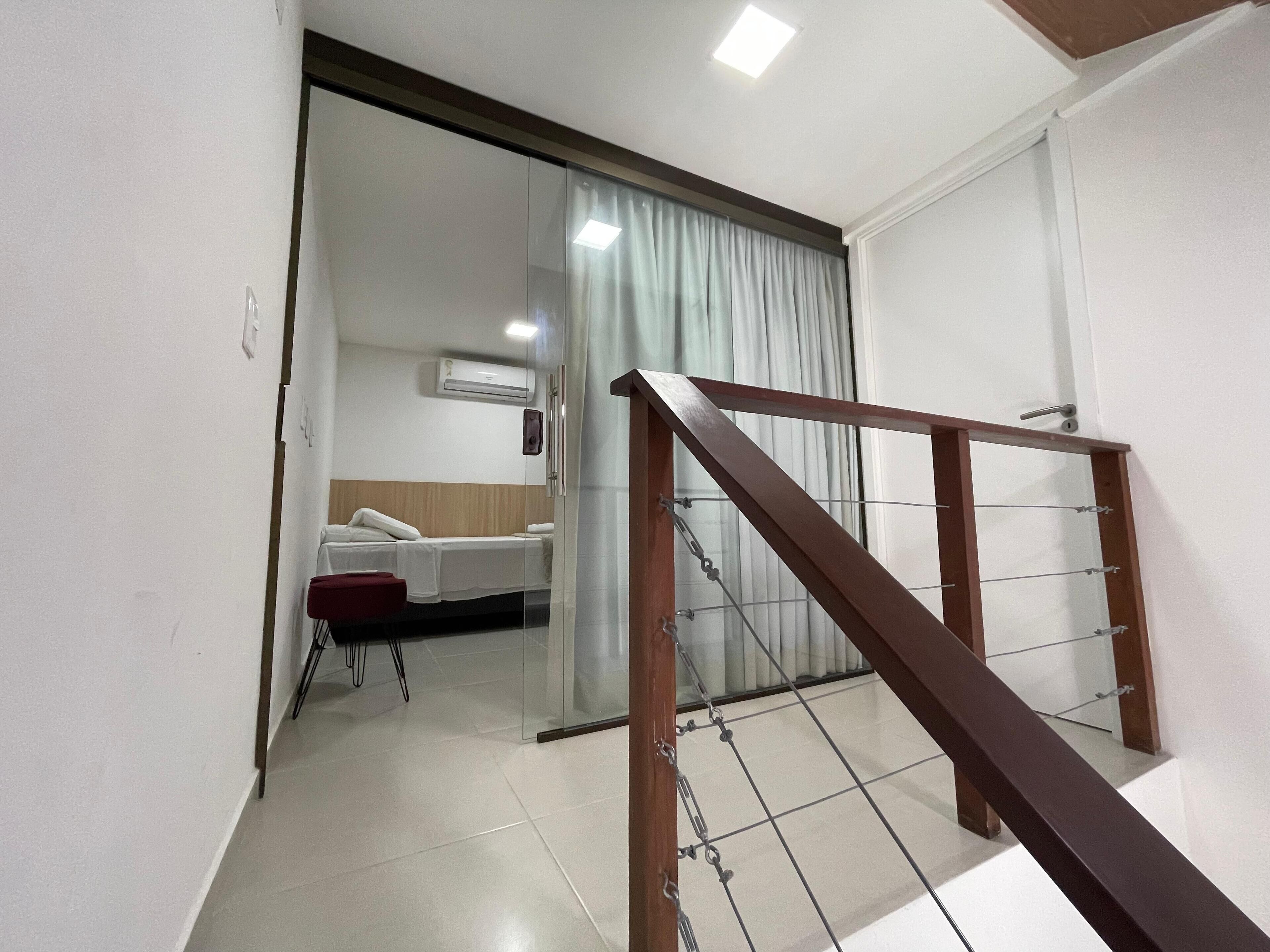 A hotel room with a bed, a small table, and a chair. There is a sliding glass door leading to another room.