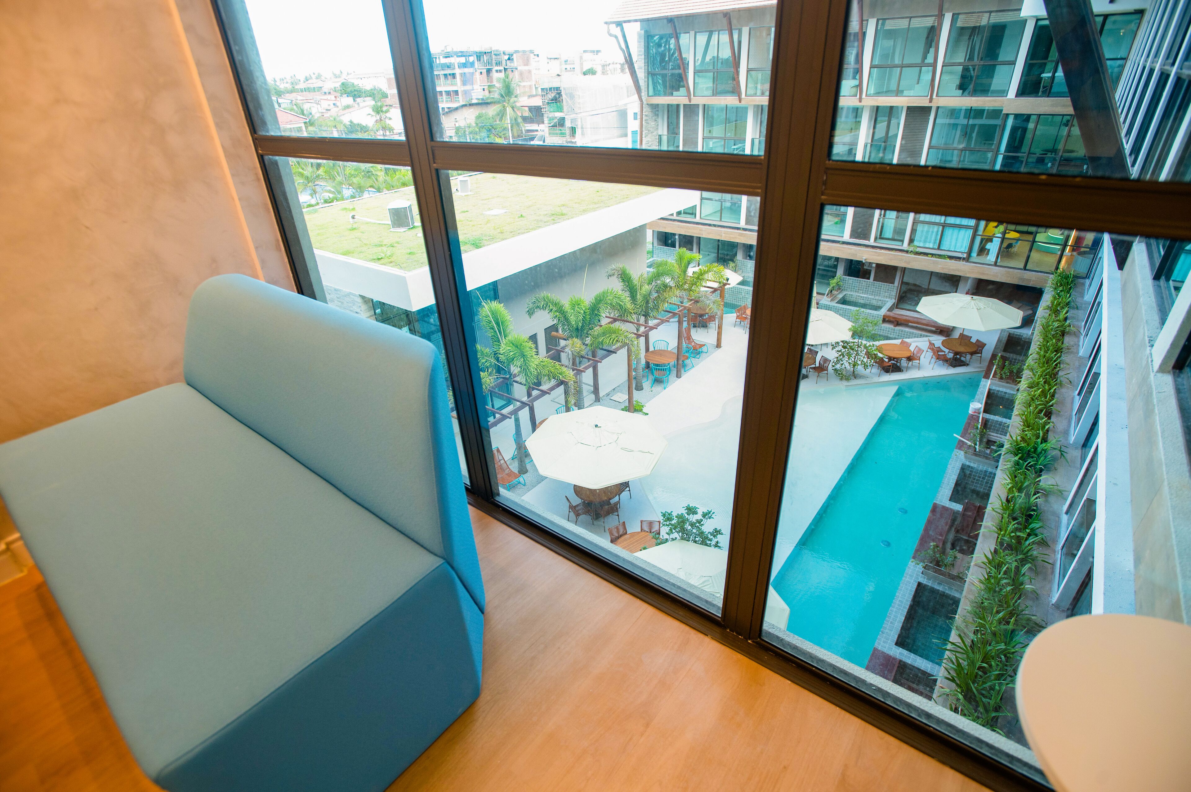 A modern hotel room with a large window overlooking a swimming pool and outdoor seating area.