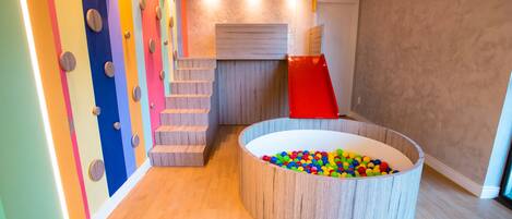 A play area with a ball pit, colorful climbing wall, and a slide.