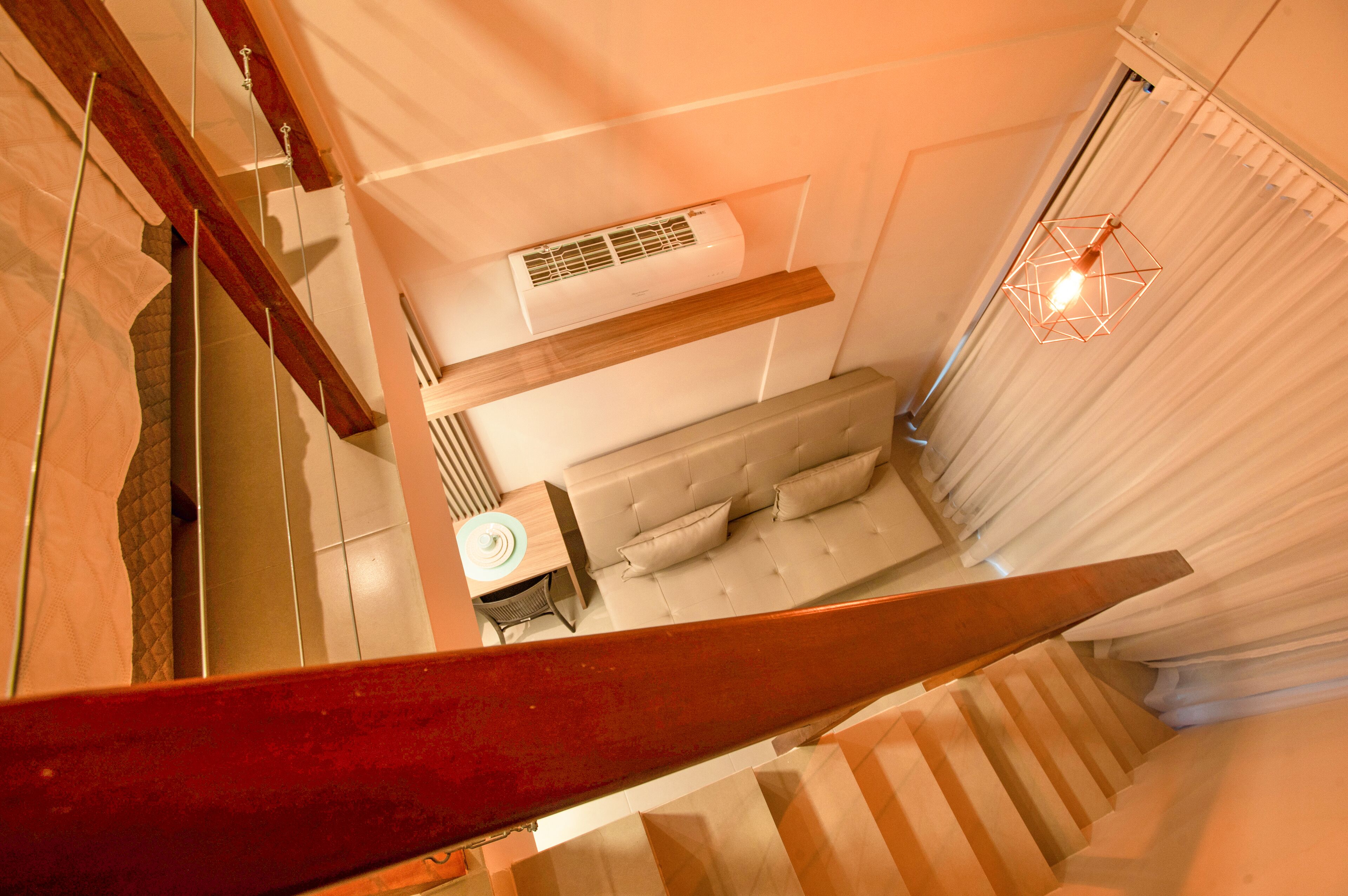 A staircase leading to a bedroom with a bed, an air conditioning unit, and a hanging light fixture.