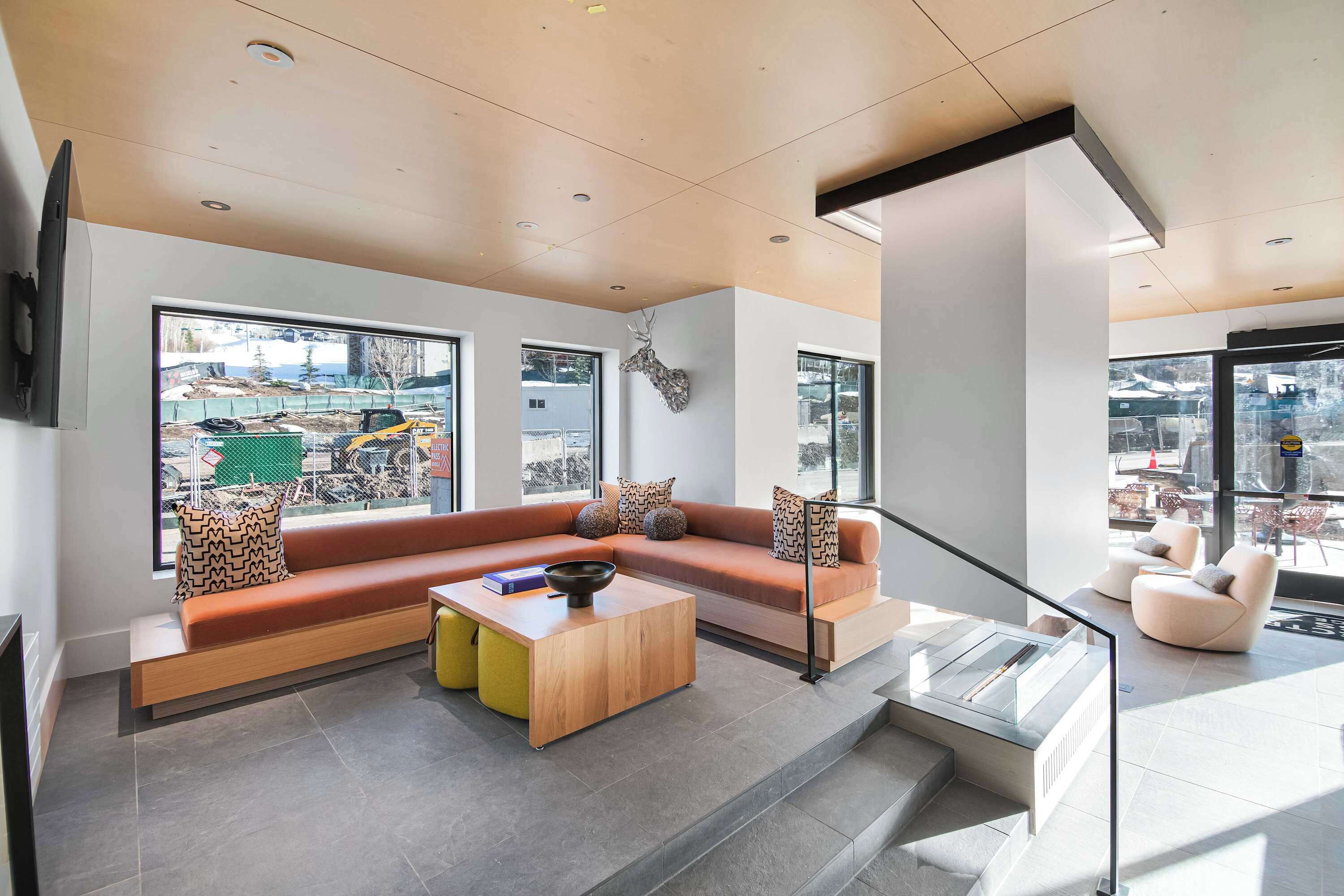 A modern living room with a sectional sofa, a coffee table, and a large window offering a view of a construction site.