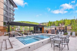 A rooftop pool area with a covered seating area, outdoor furniture, and a view of the surrounding landscape.
