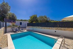 Une piscine bordée d’un mur en pierre, avec des chaises longues et une pergola.