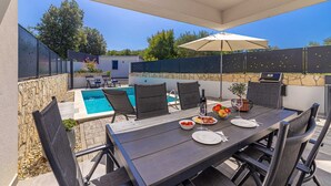 An outdoor patio with a pool, dining table, chairs, and a grill. - Villa LARUS with private pool (Malinska)