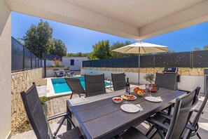 Eine Außenpatio mit Pool, Esstisch, Stühlen und Grill.