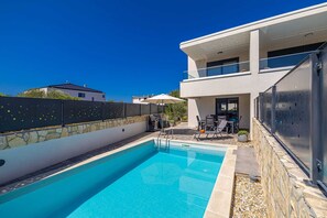 Ein modernes, zweistöckiges Haus mit Swimmingpool, Sitzgelegenheit im Freien und einer Steinmauer.