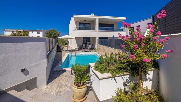 A modern two-story house with a swimming pool, outdoor seating, and a garden with pink flowers. - Villa LARUS with private pool (Malinska)