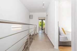 Un couloir d’hôtel moderne avec un escalier, un lit avec une literie blanche et une vue sur l’extérieur.
