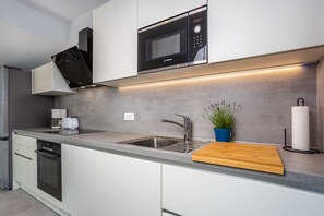 A modern kitchen with a built-in microwave, stainless steel sink, and a wooden cutting board.