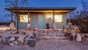 Una casa moderna con una puerta azul claro, escalones de piedra y un pequeño jardín con rocas y un árbol.