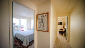 Habitación de hotel con cama, alfombra estampada y pasillo que conduce a una zona de estar con una silla y una mesita.