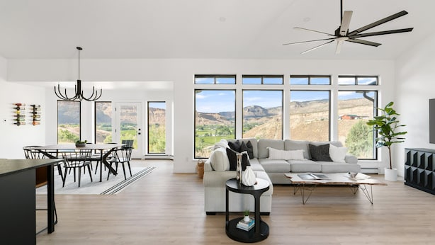 A spacious living area with a large window offering a view of the countryside, a modern kitchen with a dining table, and a ceiling fan. - The Mesa ViewHouse – Private Pool & Stunning Views – 3BR/3.5BA (Palisade)