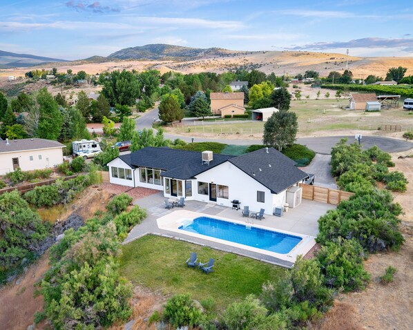 Una casa de dos pisos con piscina, rodeada por un patio cercado y un paisaje montañoso.