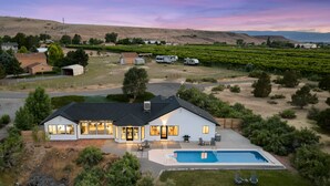A modern house with a large backyard, a swimming pool, and a vineyard in the background. - The Mesa ViewHouse – Private Pool & Stunning Views – 3BR/3.5BA (Palisade)