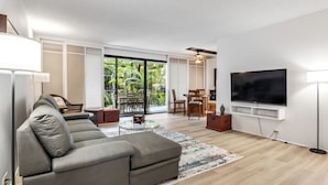 Ein modernes Wohnzimmer mit einem grauen Ecksofa, einem flachbildfernseher an der Wand und einem Essbereich mit Tisch und Stühlen.