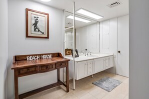 Une salle de bain avec un banc en bois, un grand miroir et un tableau encadré au mur.