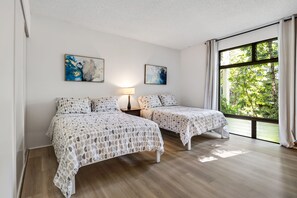 A bedroom with two beds, a nightstand, a lamp, and two abstract paintings on the wall.