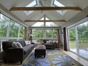 Enjoy expansive views of the surrounding greenery from large windows in this room, featuring a high ceiling and cozy seating area.