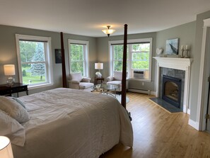 Cozy retreat with a large bed, fireplace, and windows offering views of the outdoors.