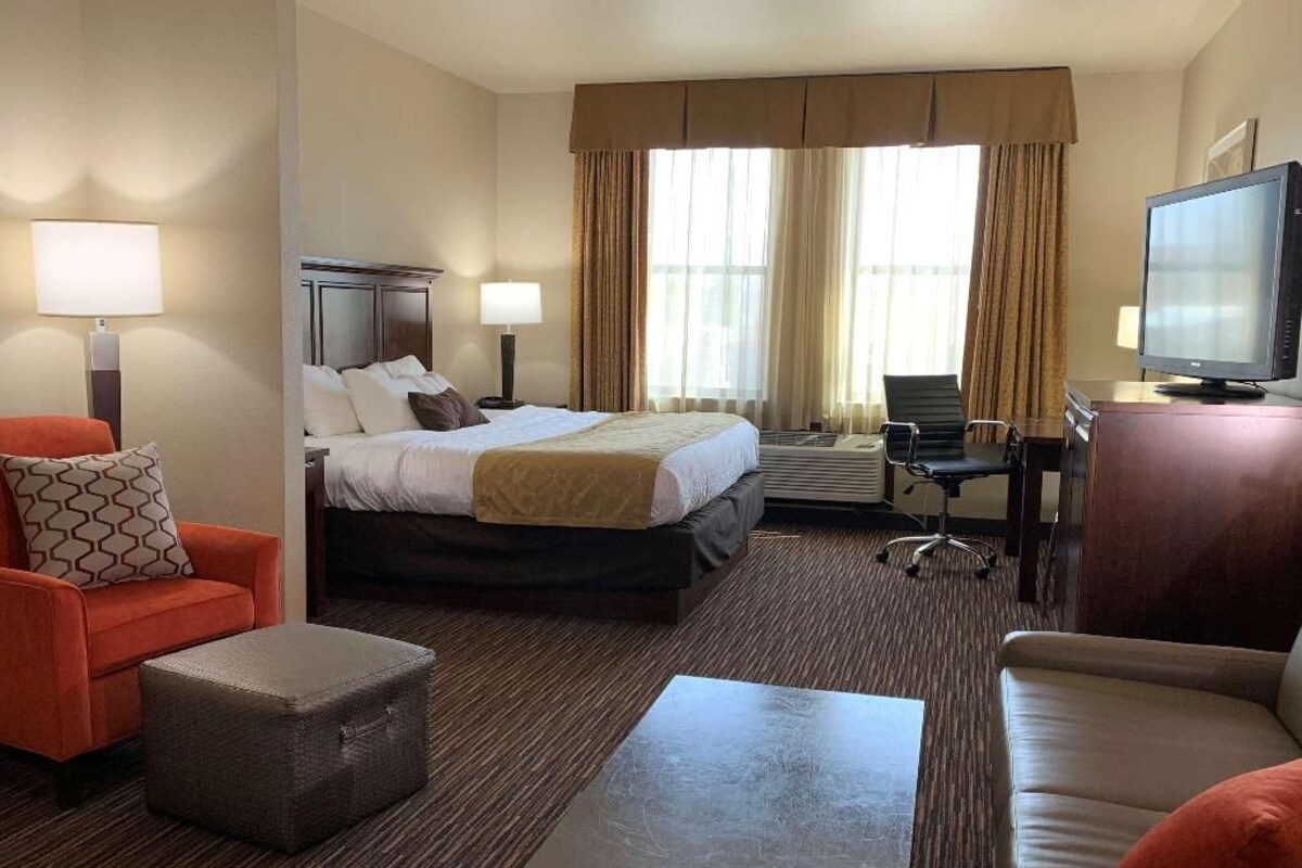 A hotel room with a bed, two armchairs, a coffee table, a television, and a desk with a chair.