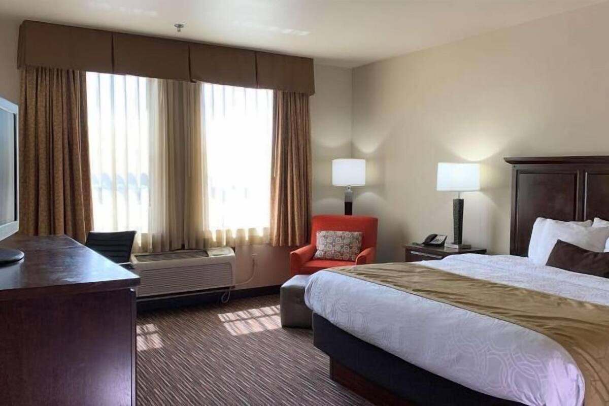 A hotel room with a bed, a desk with a TV, a chair, two bedside lamps, and a window with curtains.