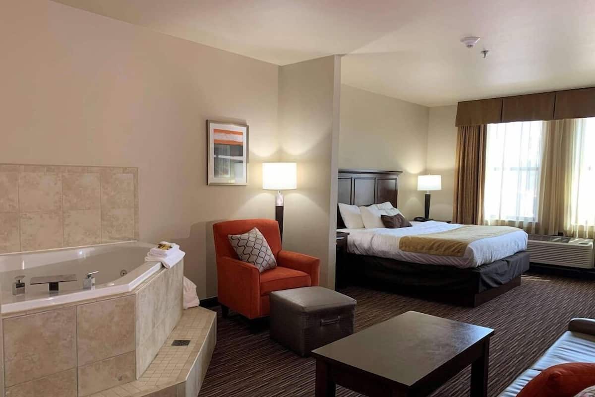 A hotel room with a bathtub, a bed, a chair, a table, and a window with curtains.