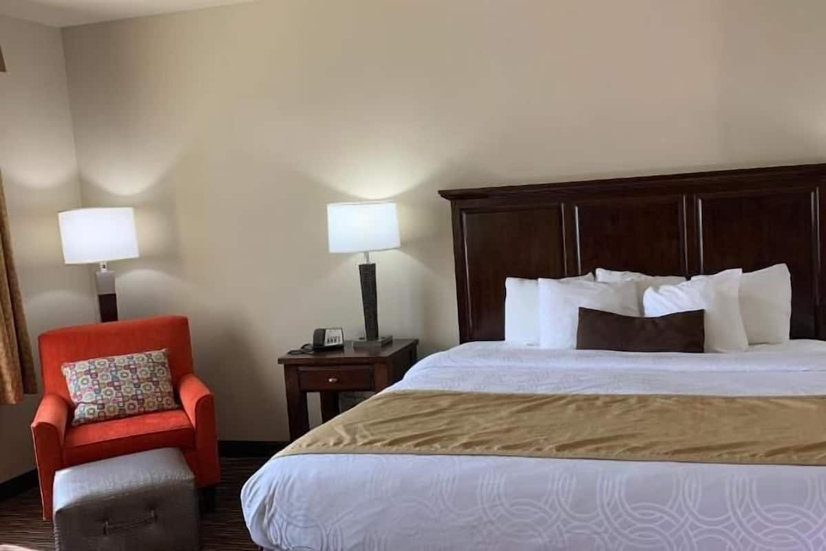 A hotel room with a large bed, two bedside tables with lamps, a red armchair, and a small ottoman.