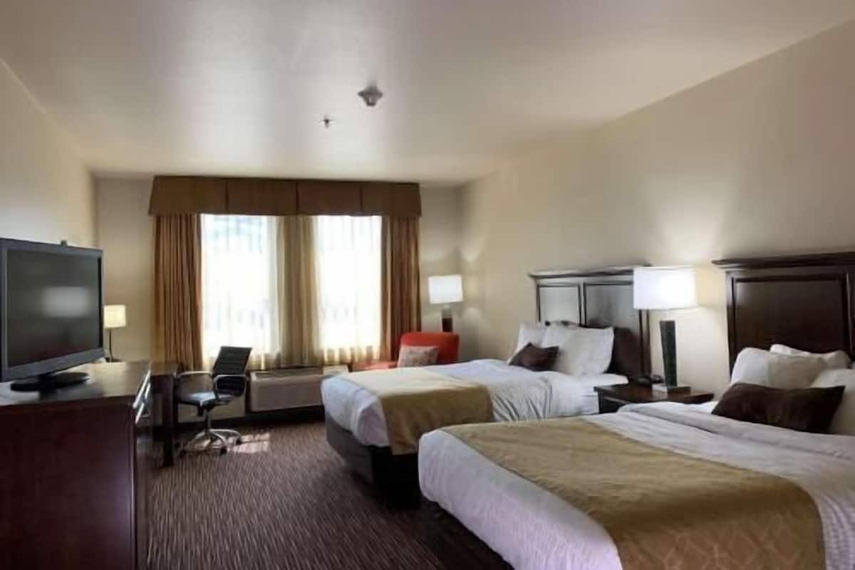 A hotel room with two beds, a TV, a desk, and a chair.