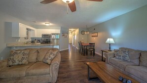 A living room with a sofa, a coffee table, and a ceiling fan. There is a kitchen area with cabinets and a microwave. - Poolside Condo in Surfside Beach (Myrtle Beach)