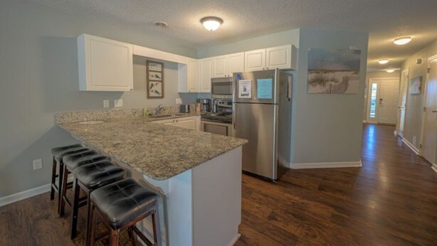 A modern kitchen with granite countertops, stainless steel appliances, and a bar stool seating area. - Poolside Condo in Surfside Beach (Myrtle Beach)