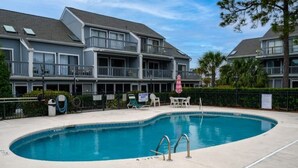 A swimming pool with a poolside area, a covered seating area, and a building with balconies in the background. - Poolside Condo in Surfside Beach (Myrtle Beach)